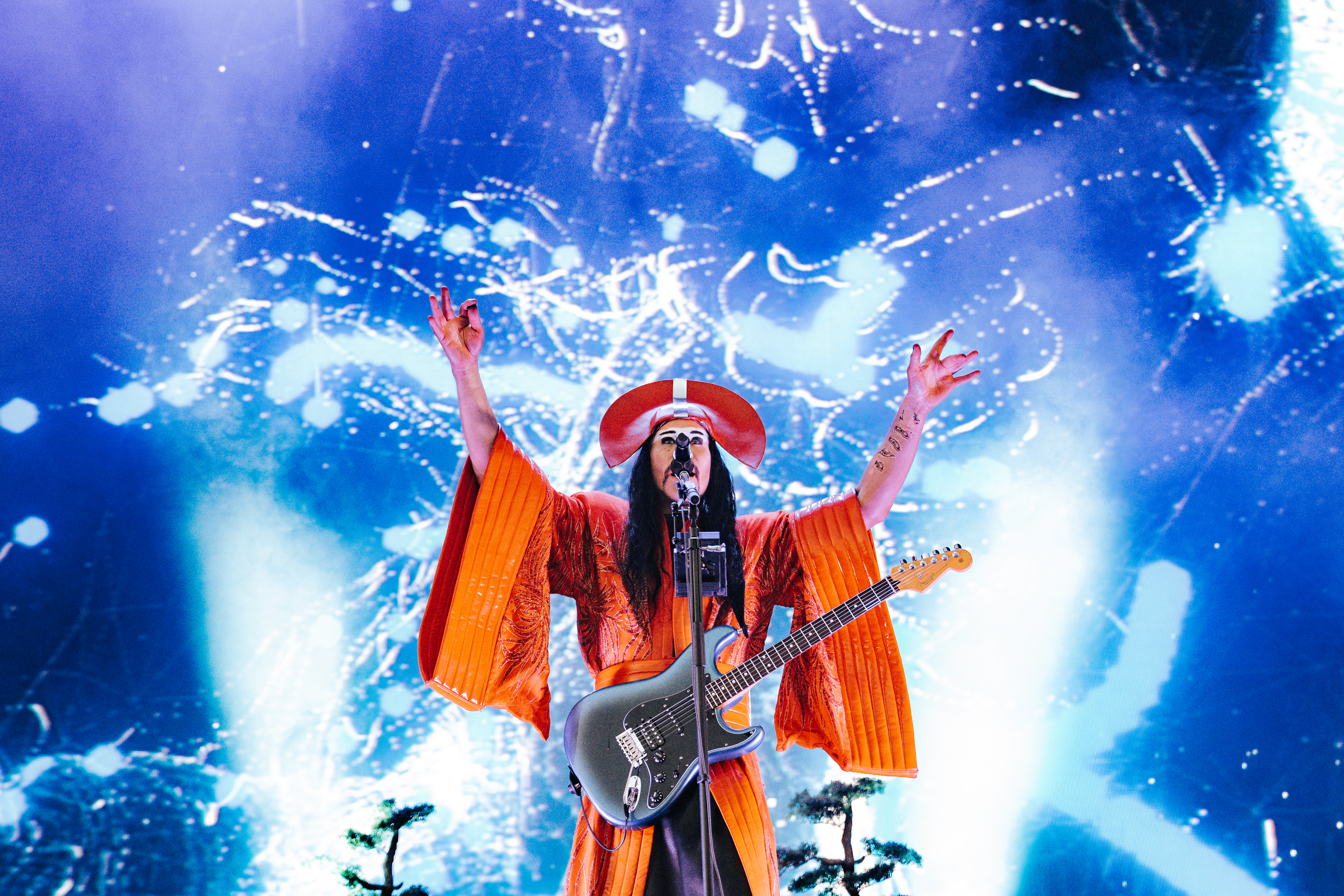 A photo of a member of the band Empire of the Sun in front of stage pyrotechnics