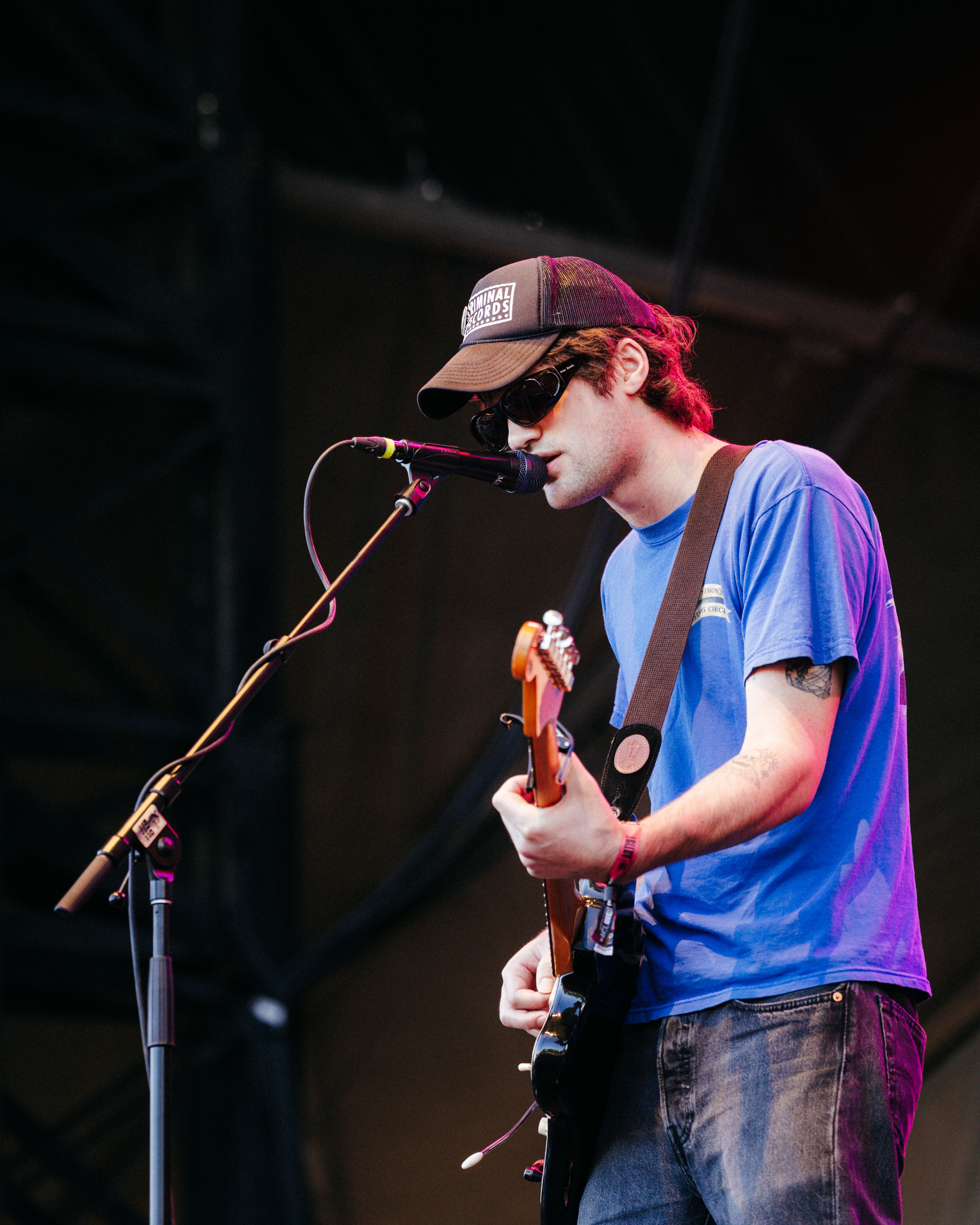 A photo of MJ Lenderman on stage playing guitar in front of a microphone